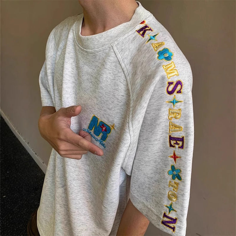 Person wearing a white sweatshirt with colorful embroidered letters on the sleeves.